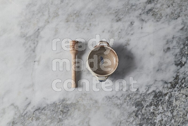 Multicolored pottery bowl with wooden honey dipper on the side on grey marble background