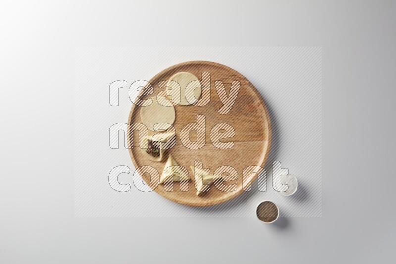 two closed sambosas and one open sambosa filled with meat while salt and black pepper aside in a wooden dish on a white background