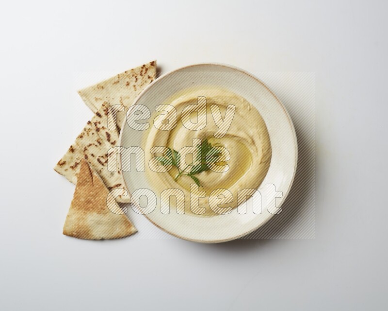 Hummus in a pottry plate garnished with parsley on a white back ground