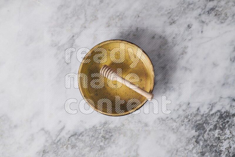 Multicolored pottery oven plate with wooden honey dipper in it on grey marble background