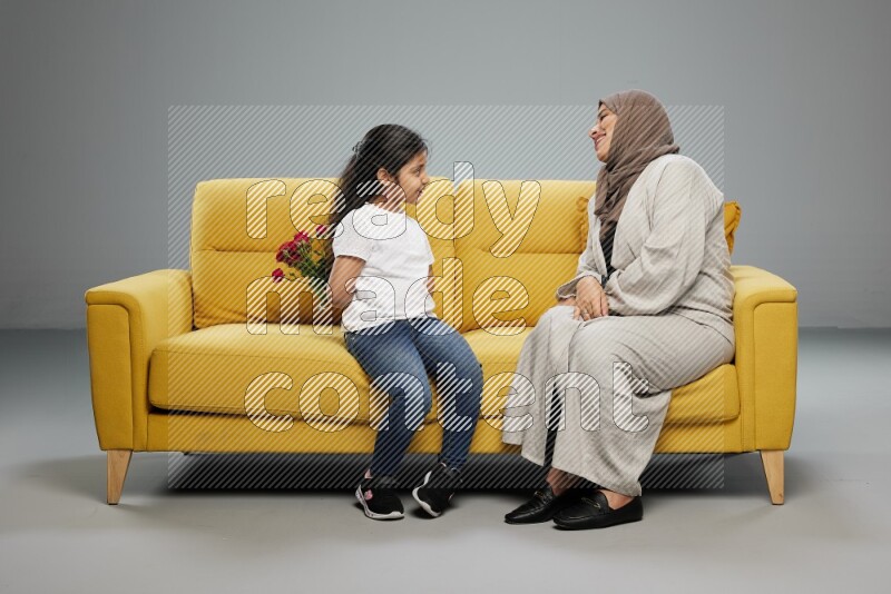 A girl sitting hiding flowers behind her back for her mother on gray background