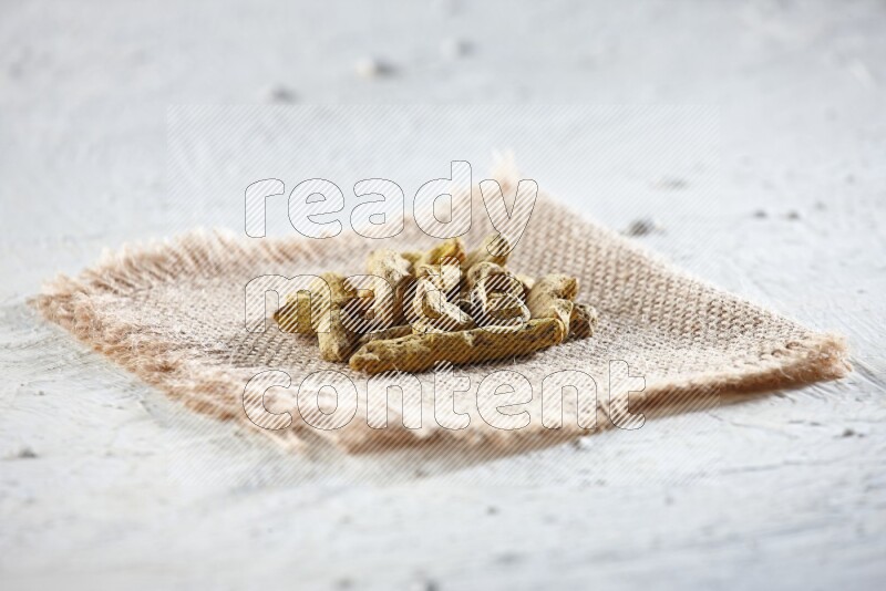 Dried turmeric whole fingers on a piece of burlap on a textured while flooring