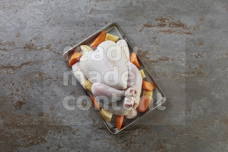 whole Raw chicken on a small oven trey direct on a rustic grey background