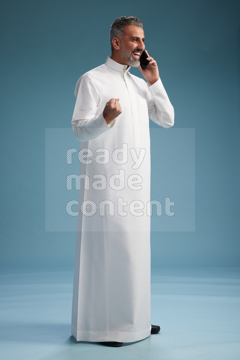 Saudi man wearing thob talking on the phone on blue background