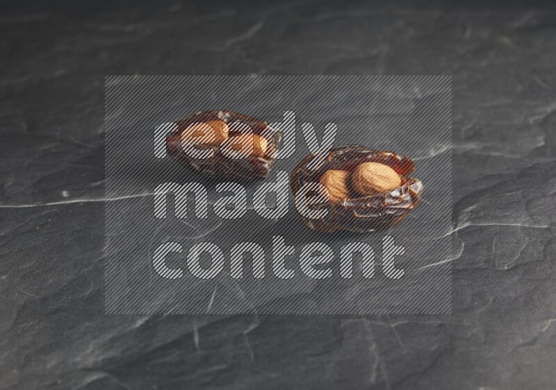 two almond stuffed madjoul dates on a black textured background