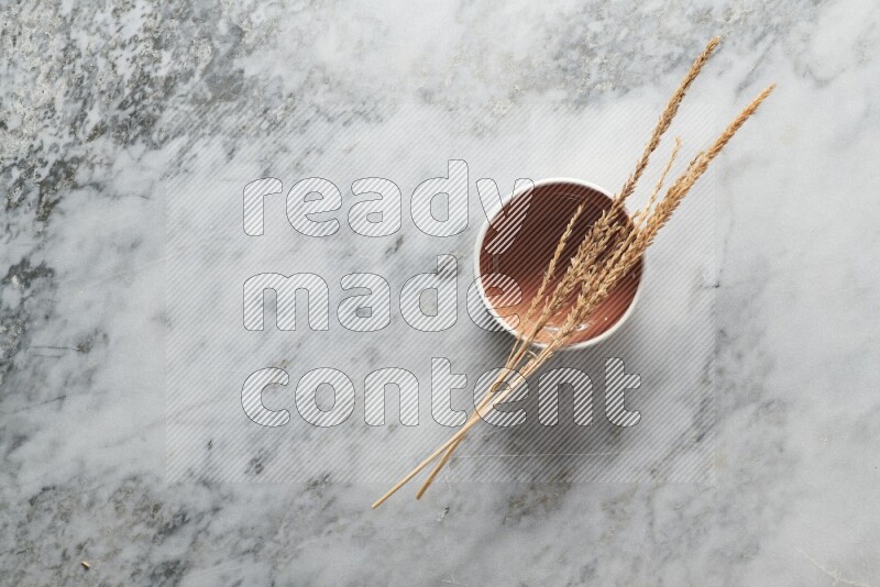 Wheat stalks on brown pottery bowl on grey marble background