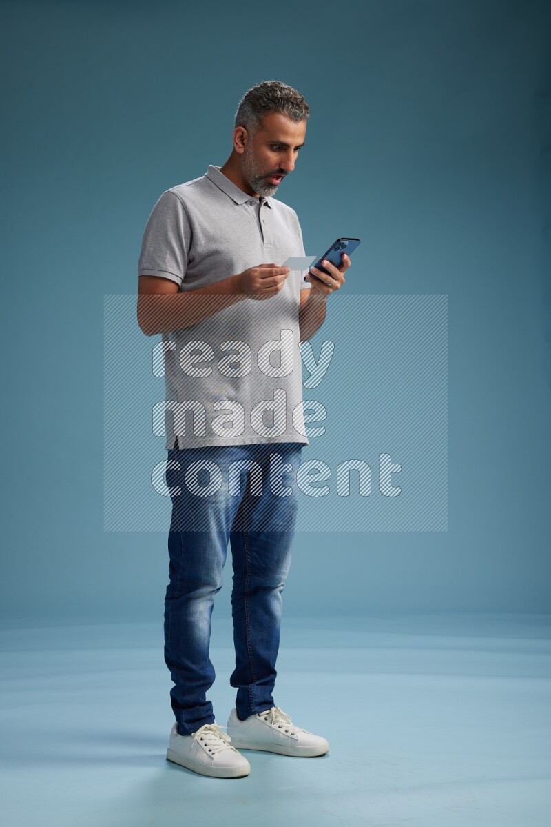 Man Standing holding ATM while talking on phone on blue background
