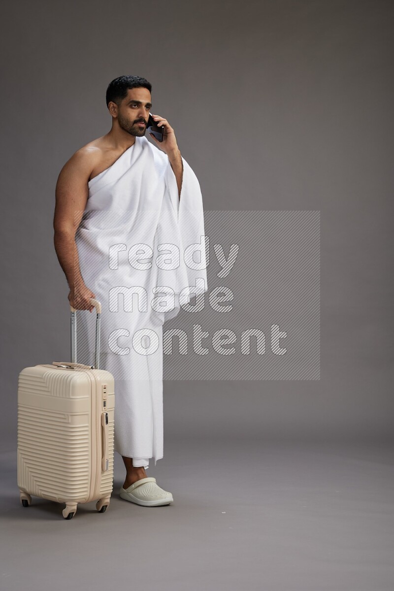 A man wearing Ehram Standing holding traveling bag on gray background