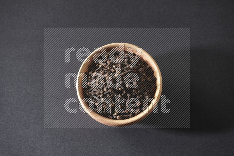 A wooden bowl full of cloves on a black flooring