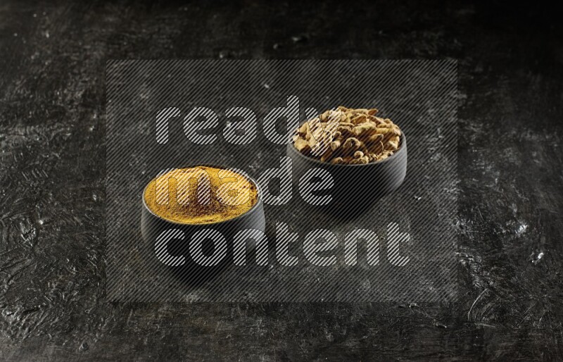 وعاءان من الفخار باللون الأسود، أحدهما ممتلئ ببودرة الكركم والآخر ممتلئ بأصابع كاملة من الكركم المجفف على خلفية سوداء