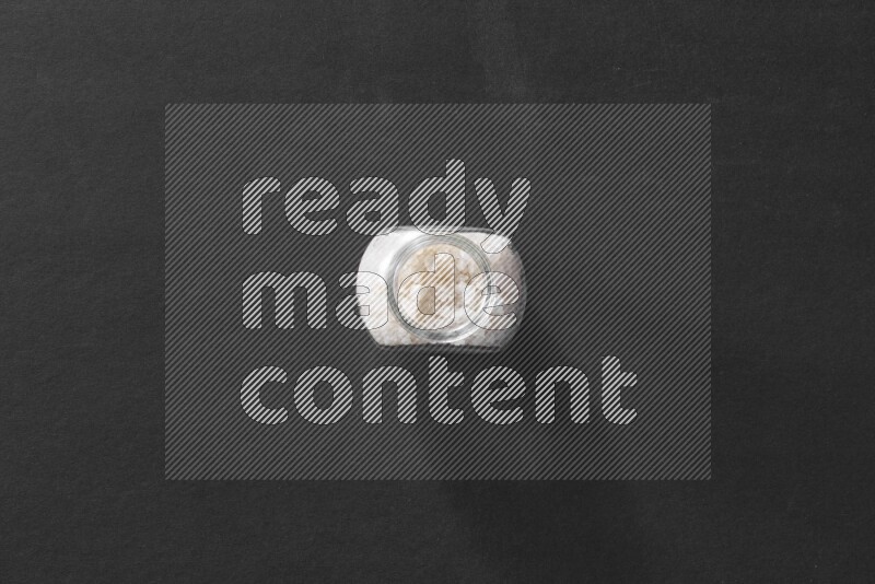 A glass spice jar full of salt on black flooring