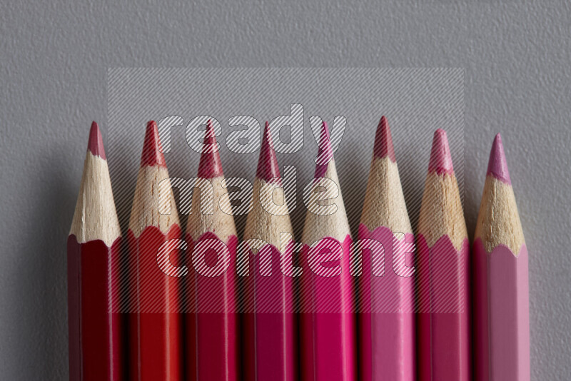A collection of colored pencils arranged showcasing a gradient of pink and red hues on grey background