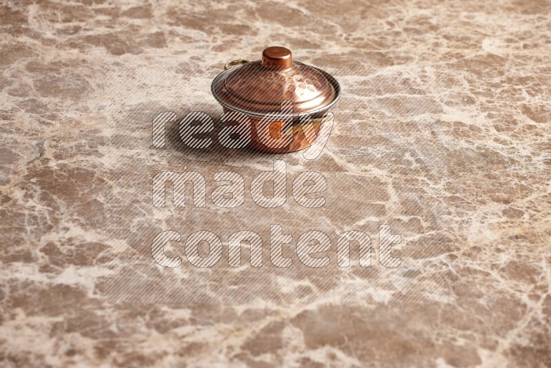 A small copper pot on beige marble background