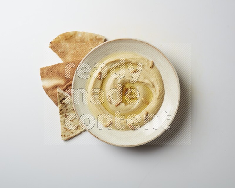 Hummus in a pottry plate garnished with pine nuts on a white background