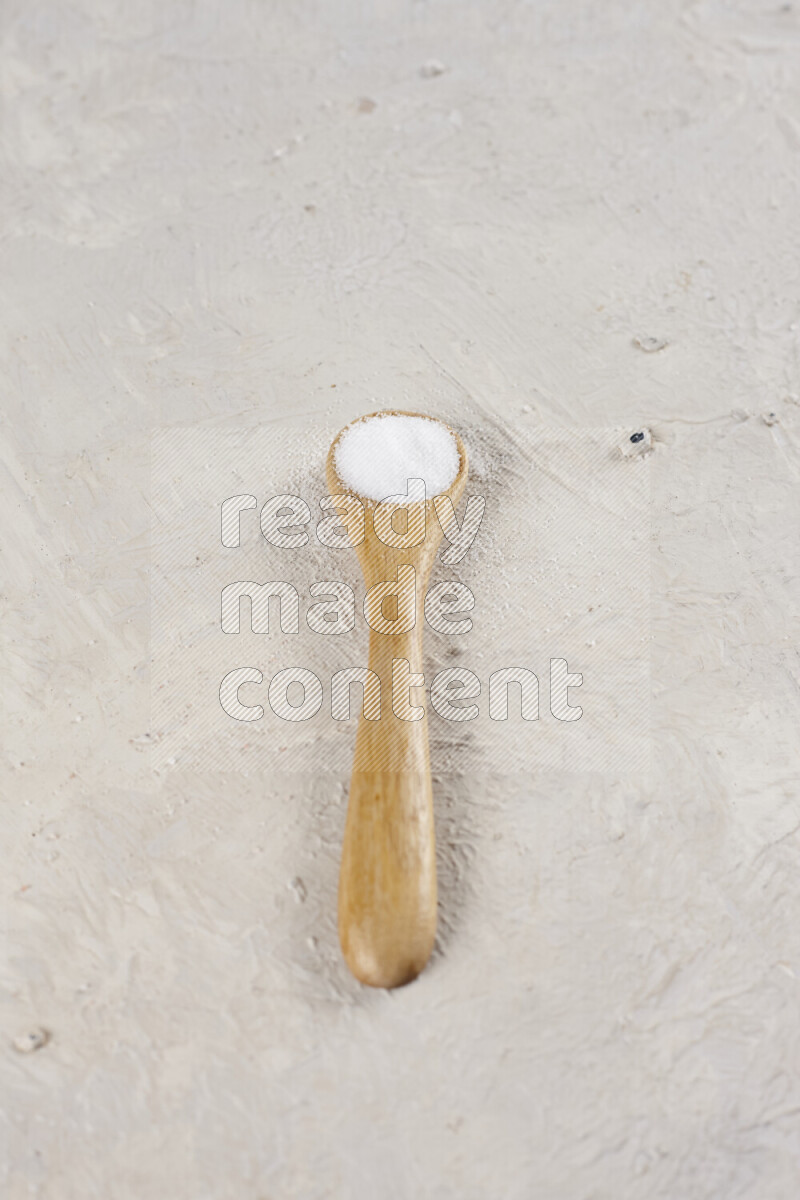 A wooden spoon full of white salt on white background