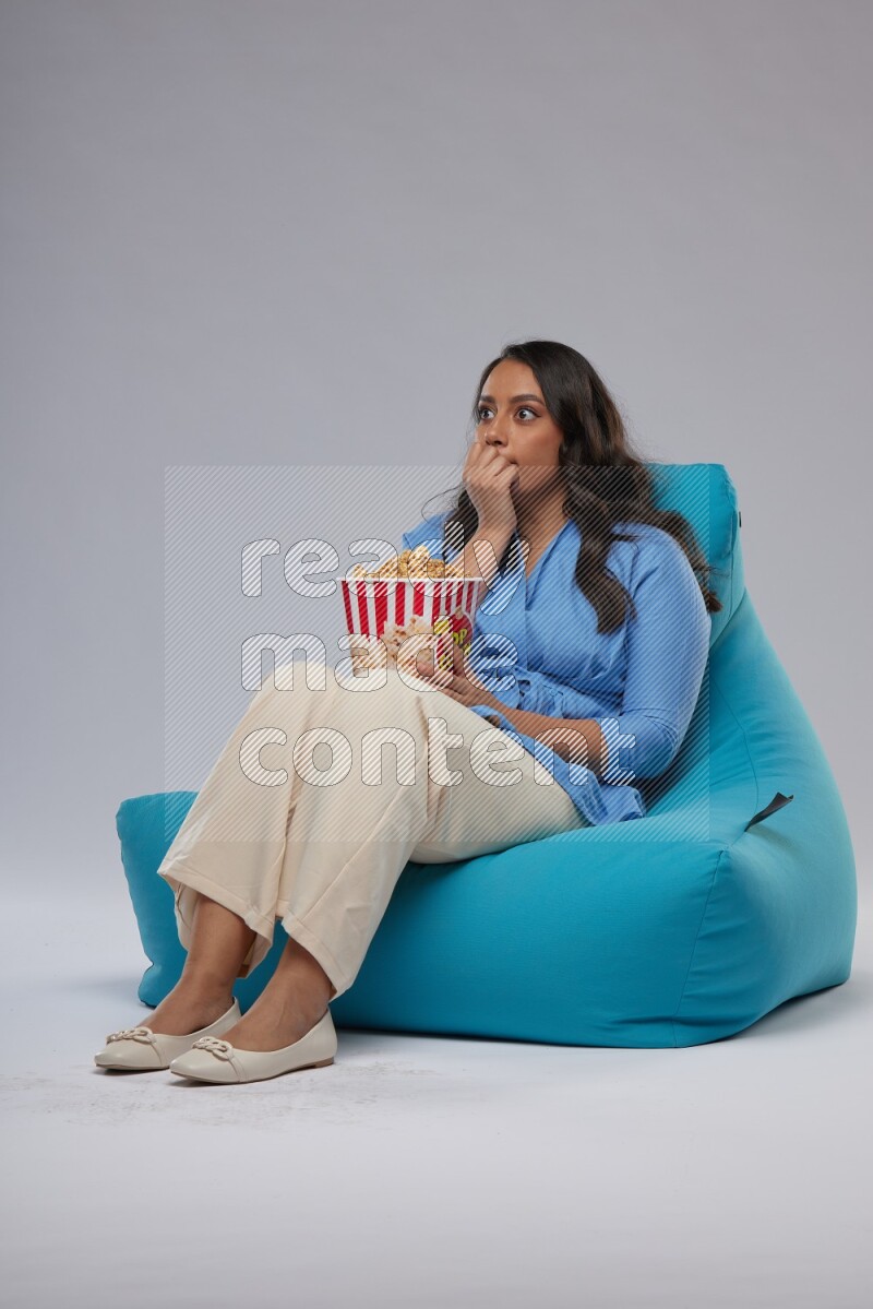 A woman sitting on a blue beanbag and eating popcorn