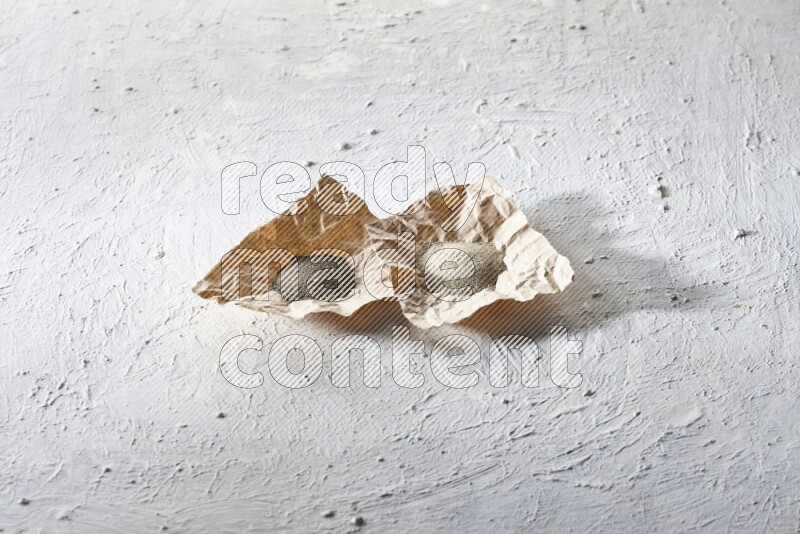 2 Crumpled pieces of paper full of black and white pepper powder on a textured white flooring