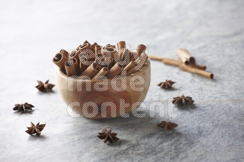 wooden bowl full of cinnamon sticks surrounded by star anis on marble background in different angles