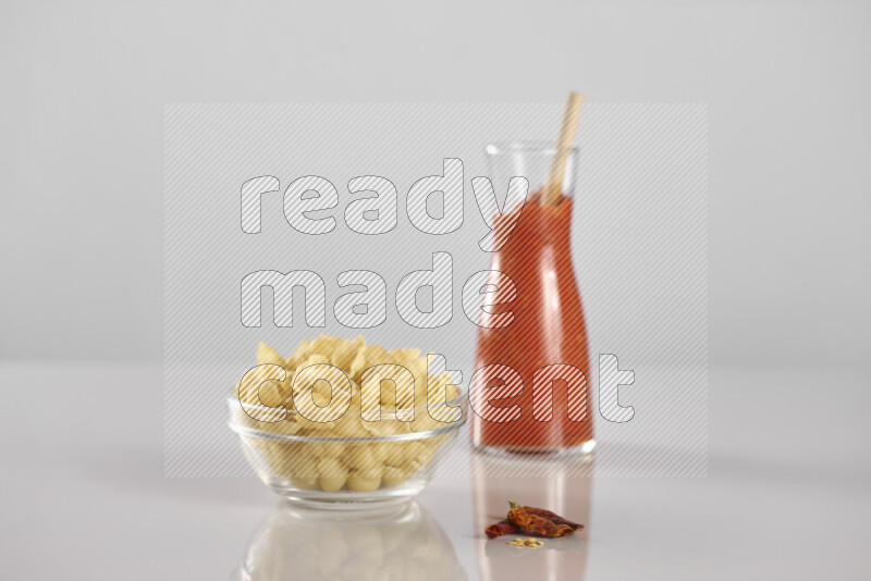 Raw pasta with tomatoe pasta with different ingredients such as cherry tomatoes, basil, garlic, bay laurel, cardamom, white pepper, black pepper, red chilis and wheat stalks on light grey background