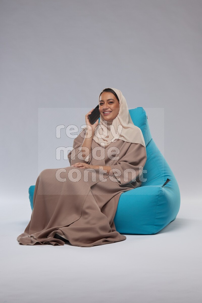 A Saudi woman sitting on a blue beanbag and working on laptop