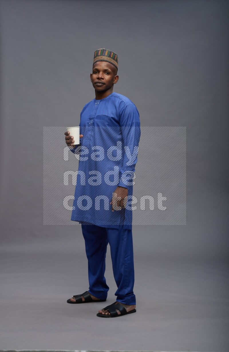 Man wearing Nigerian outfit standing holding paper cup on gray background
