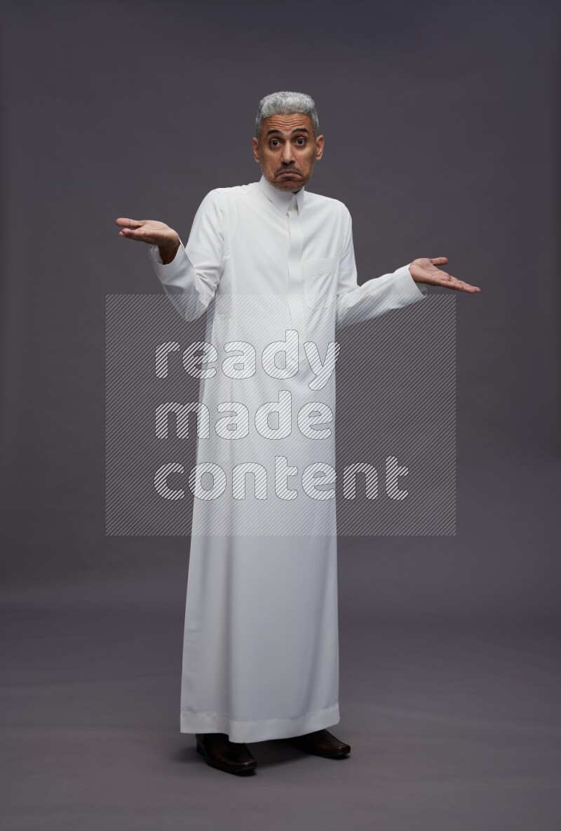Saudi man wearing thob standing interacting with the camera on gray background