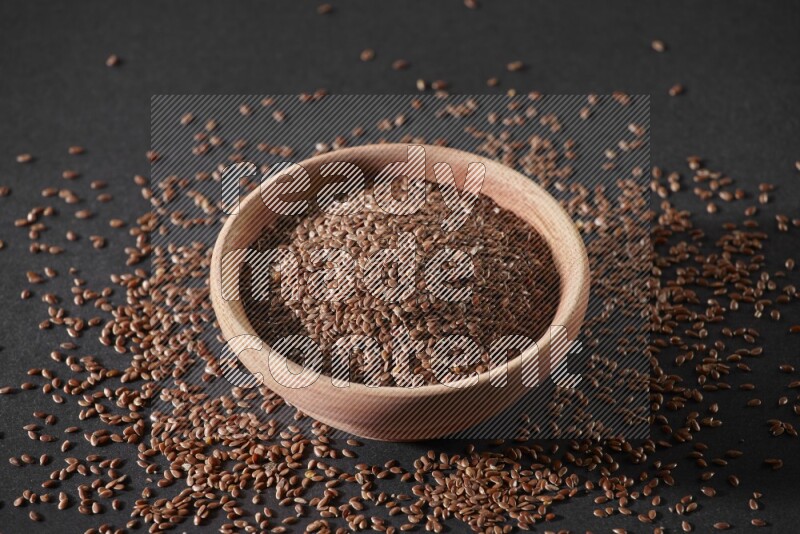 A wooden bowl full of flax surrounded by the seeds on a black flooring in different angles
