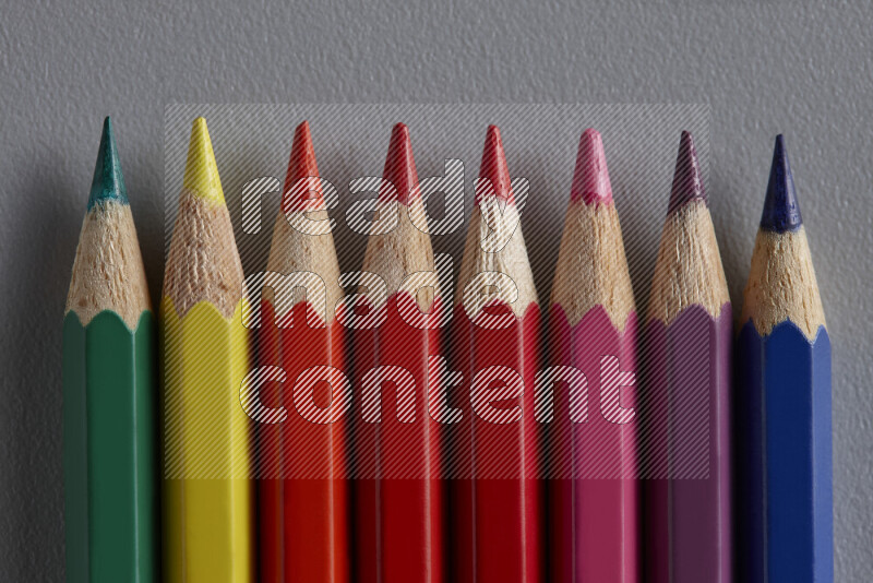 A collection of colored pencils arranged showcasing a gradient of different hues on grey background