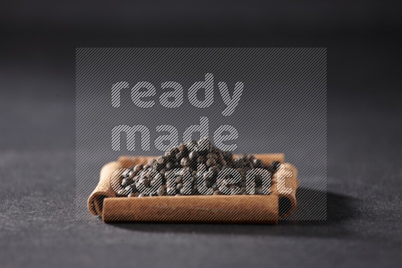 أربعة من أعواد القرفة مكونة شكل مربع بداخلها حبوب الفلفل الأسود علي خلفية سوداء