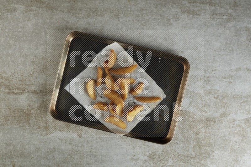 wedges potato on parchment paper in a black stainless steel rectangle tray on grey textured counter top