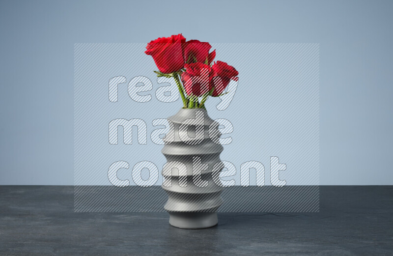 An arrangement of vivid red roses in a grey spiral vase on black marble background