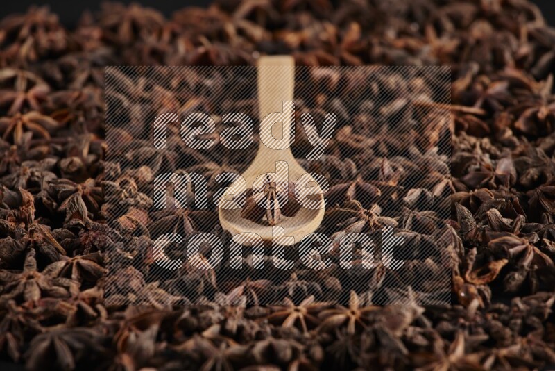 اليانسون النجمي في ملعقة خشبية فوق اليانسون النجمي الذي يغطي الإطار على أرضية سوداء