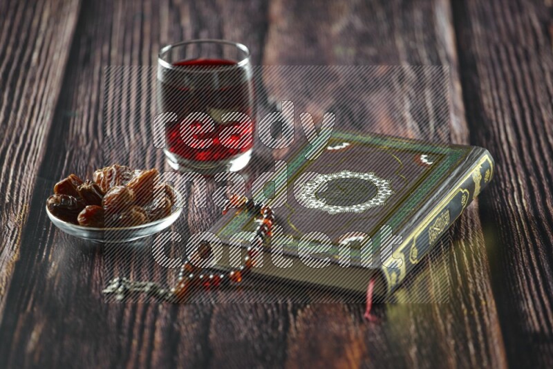 Quran with dates, prayer beads and different drinks all placed on wooden background