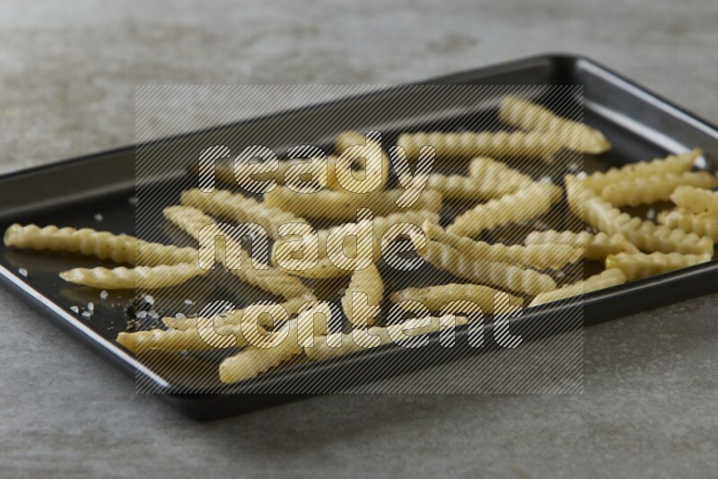 crinkle fries in a black stainless steel rectangle tray on grey textured counter top