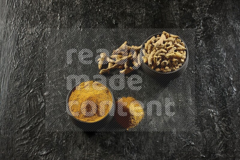 وعاءان من الفخار باللون الأسود، أحدهما ممتلئ ببودرة الكركم والآخر ممتلئ بأصابع كاملة من الكركم المجفف على خلفية سوداء