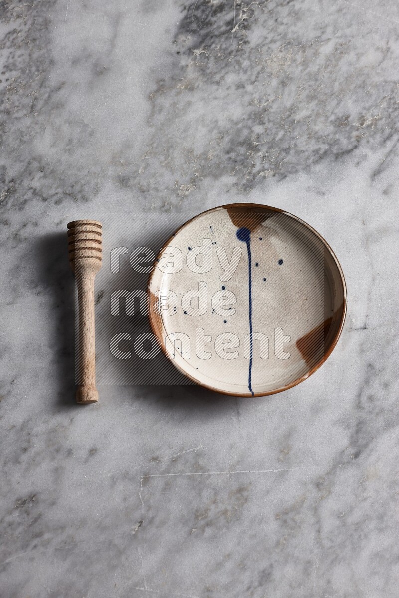 Multicolored pottery plate with wooden honey dipper on the side on grey marble background