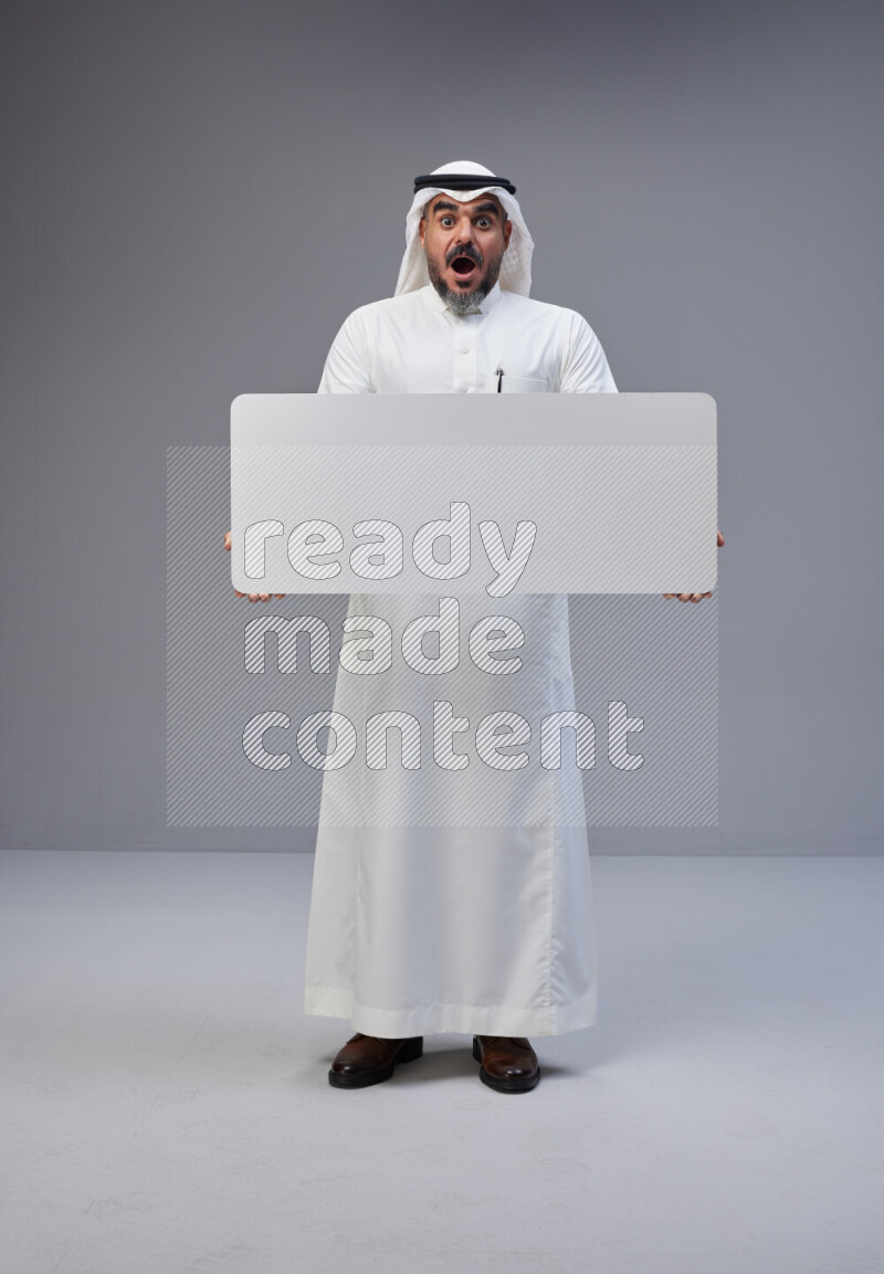 Saudi man Wearing Thob and white Shomag standing holding board on Gray background