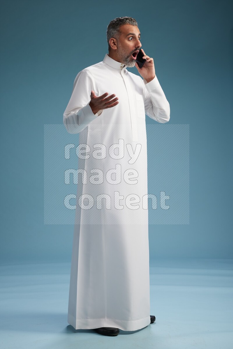 Saudi man wearing thob talking on the phone on blue background