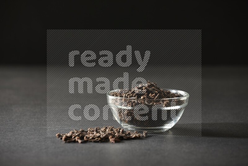 A glass bowl full of cloves on a black flooring