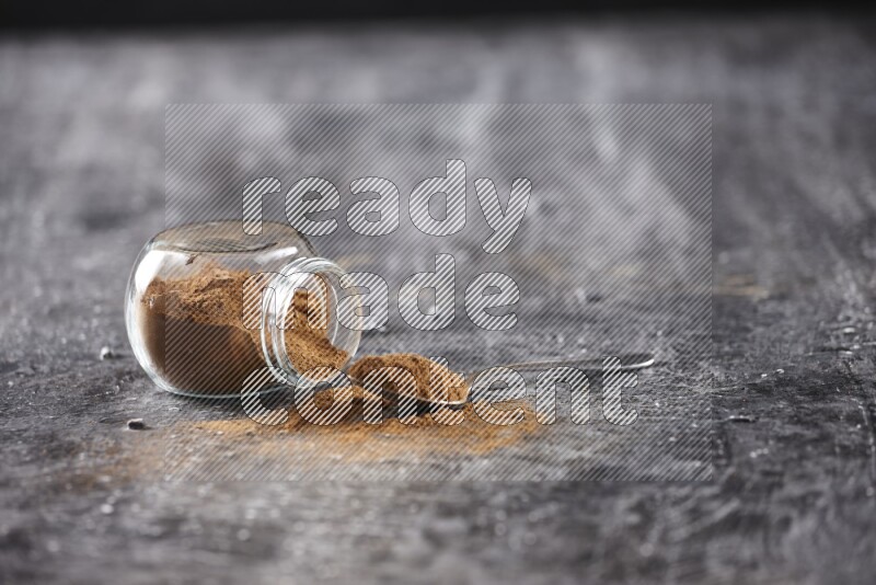 قرفة في وعاء زجاجي مقلوب مع ملعقة معدنية علي خلفية سوداء