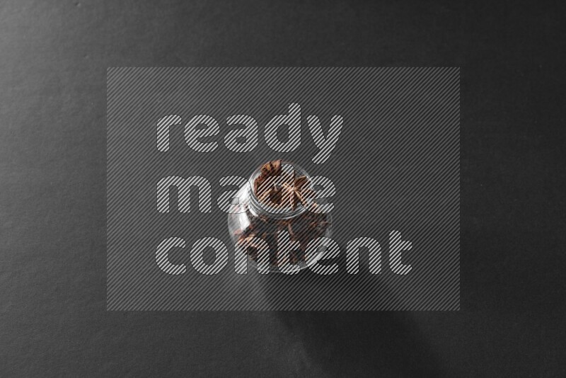 A glass spice jar full of star anise on black flooring