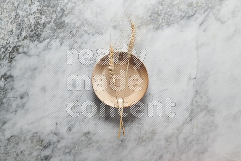 Wheat stalks on beige pottery plate on grey marble background