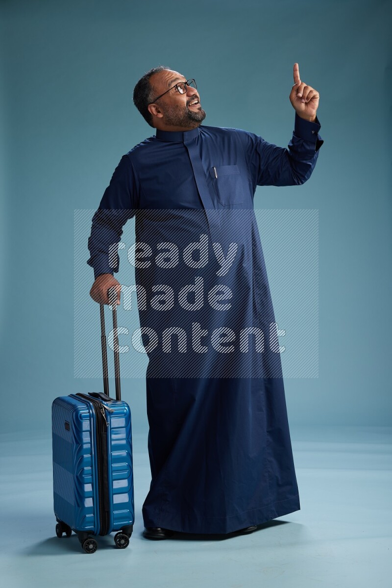 Saudi Man without shimag Standing pulling travel bag on blue background