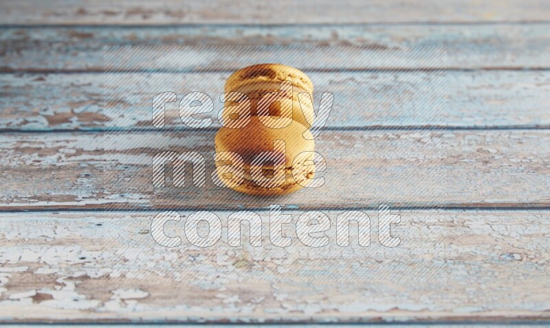 45º Shot of two Yellow Crème Brulée macarons on light blue wooden background