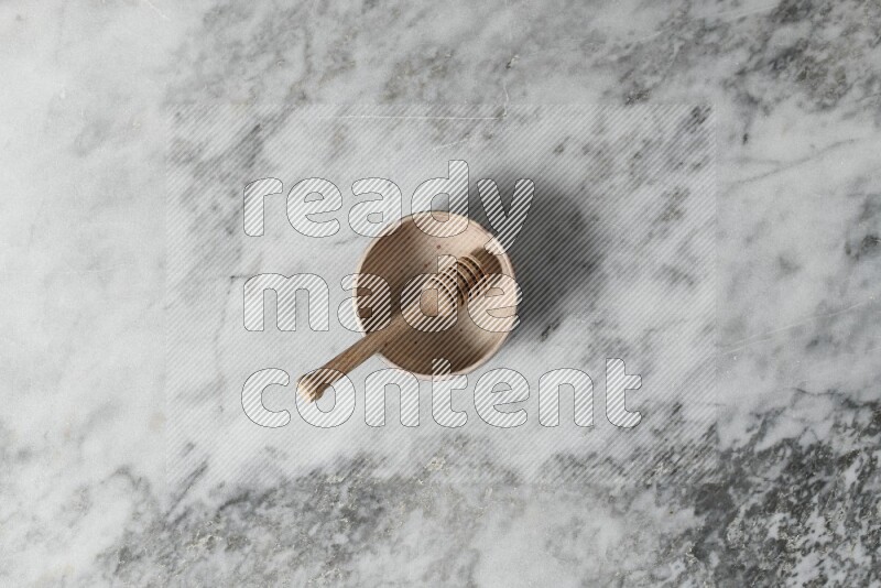 Beige pottery bowl with wooden honey dipper in it on grey marble background