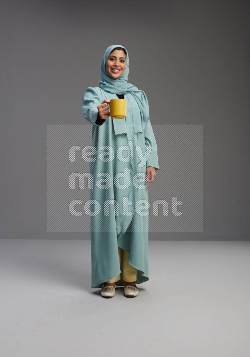 Saudi Woman wearing Abaya standing  holding a mug on Gray background