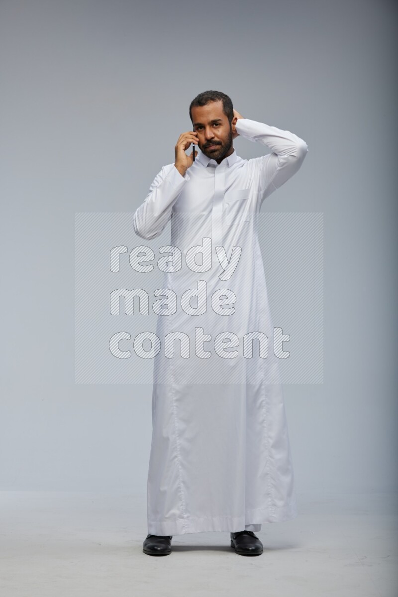 Saudi man wearing Thob standing talking on phone on Gray background