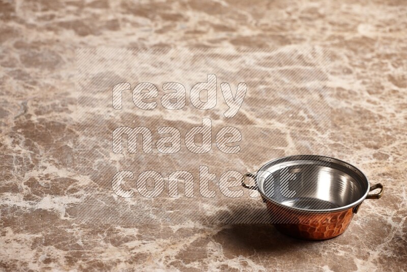 A small copper pot on beige marble background