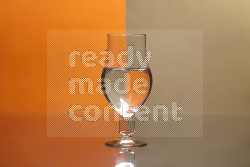 The image features a clear glassware filled with water, set against orange and beige background