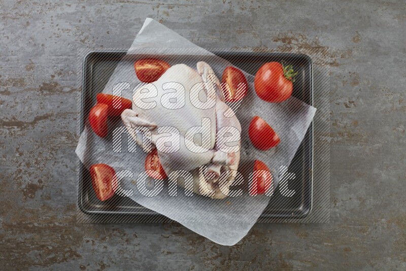 whole raw chicken on an oven trey direct on a rustic grey background